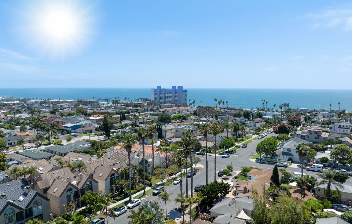 A sunny cityscape with low-rise houses under a clear blue sky, illuminated by intense sunlight
