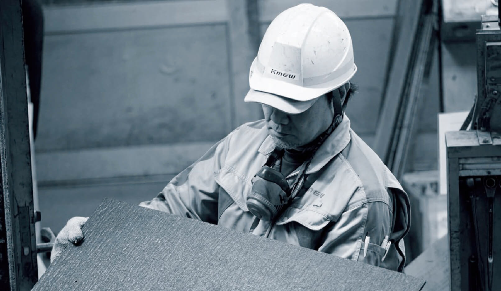 A factory worker wearing a helmet and uniform holding a KMEW siding panel